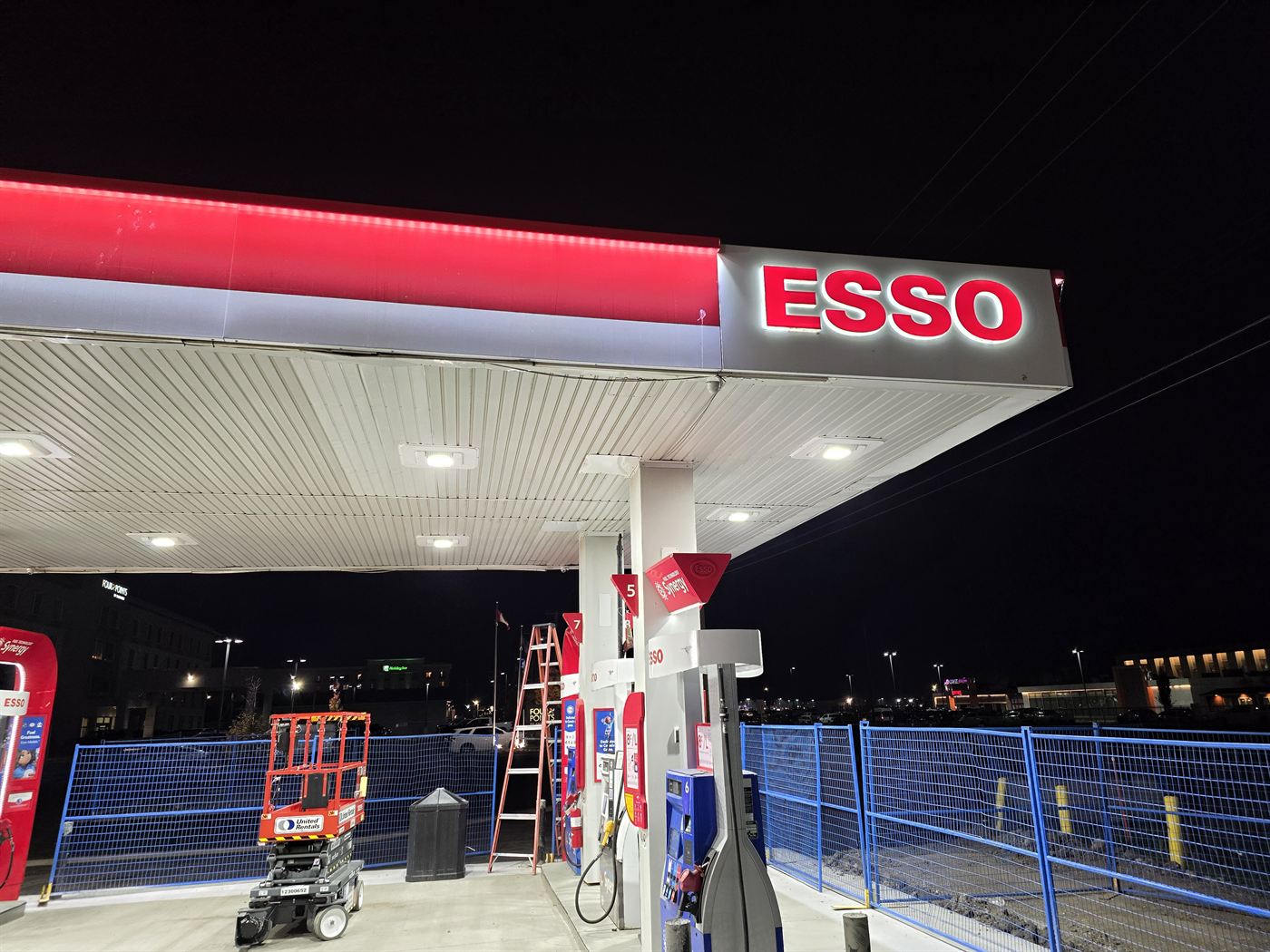 Illuminated Esso canopy sign at night with work lights and a lift on the forecourt