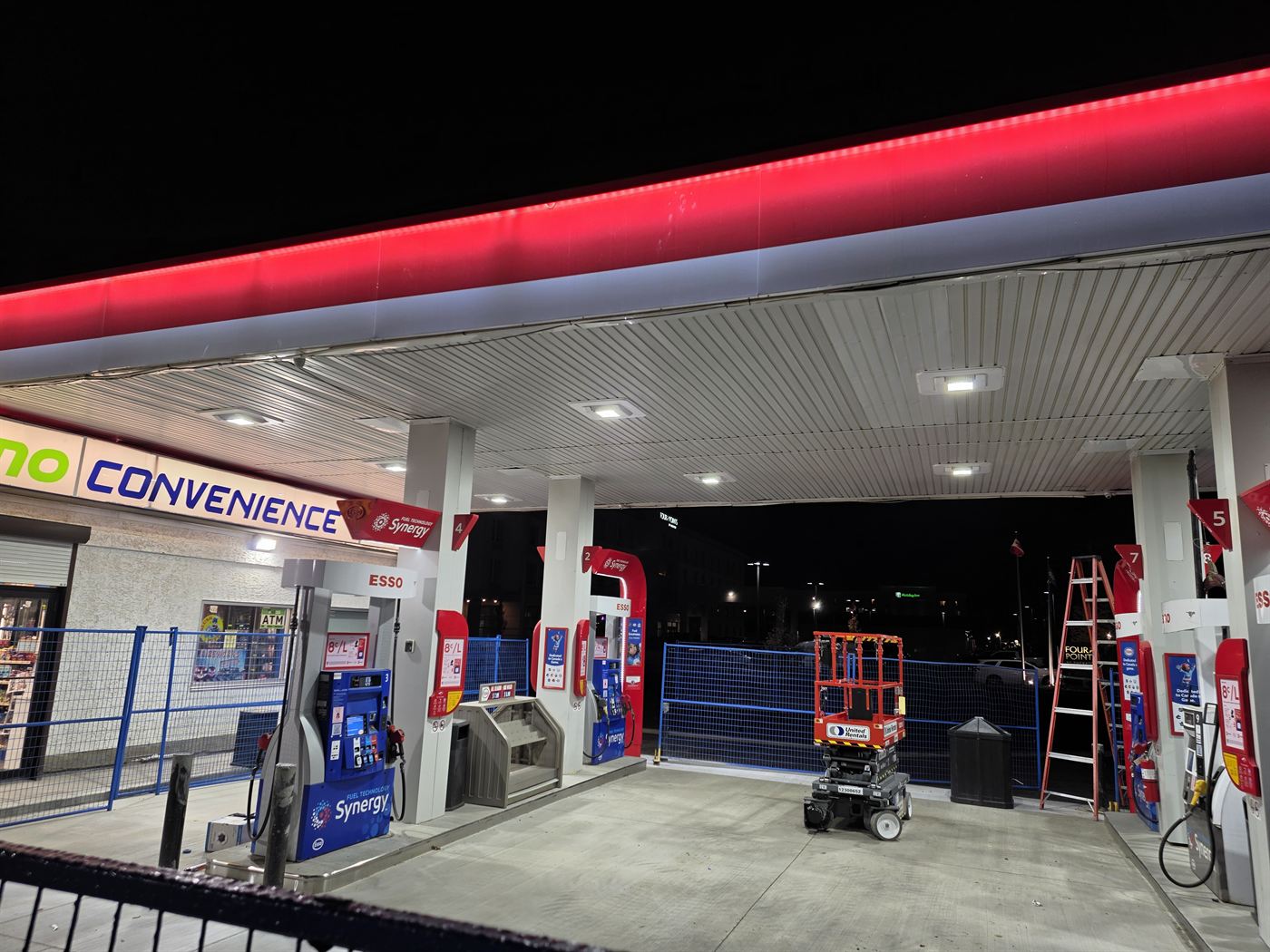 Under-canopy view of Esso fuel pumps and convenience store signage at night